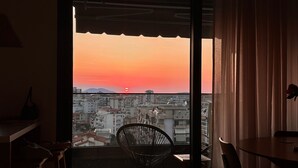 A room with a view of a sunset over a cityscape, a dining table, and a chair.