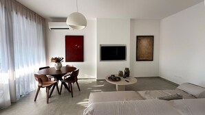 A modern hotel room with a large bed, a dining area with a round table, and a TV mounted on the wall.