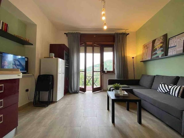 A living room with a sofa, a coffee table, a television, and a kitchen area with a refrigerator.