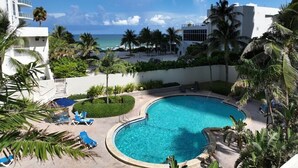 A swimming pool with lounge chairs, surrounded by palm trees and a view of the ocean. - Beachfront Condo| Steps to Broadwalk | Sleeps 6|Pool+Gym (Hollywood)