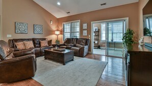 A spacious living room with leather sofas, a coffee table, and a ceiling fan.