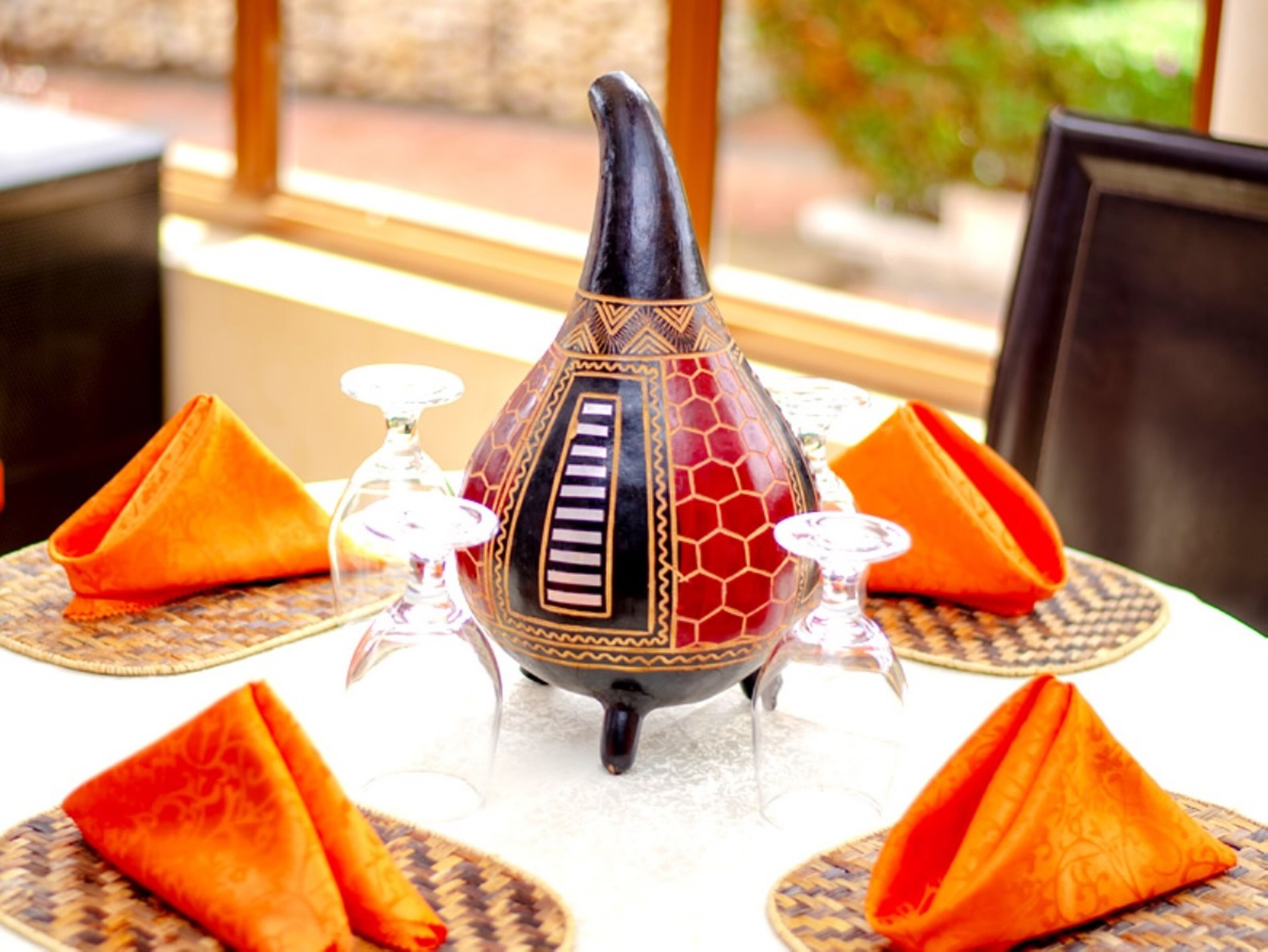 A table set with a decorative vase, orange napkins, and clear glassware.