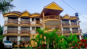 A multi-story hotel with balconies, a paved driveway, and tropical landscaping. - Hotel Lemonade (Kampala)