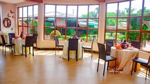 A dining area with large windows, multiple tables, and chairs. - Hotel Lemonade (Kampala)