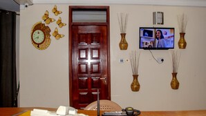 A room with a wooden door, a clock with butterfly decorations, a television mounted on the wall, and two decorative vases. - Hotel Lemonade (Kampala)