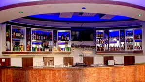 A bar area with a curved counter, multiple shelves of liquor bottles, and three red bar stools. - Hotel Lemonade (Kampala)