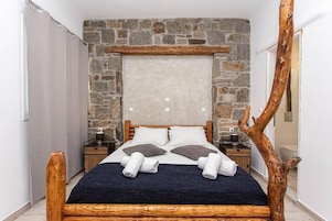 Quarto com parede de pedra, cabeceira de madeira e decoração rústica com um galho de árvore.