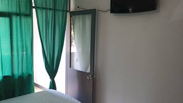 Una habitación con dos camas, un televisor en la pared y un ventanal con cortinas verdes.