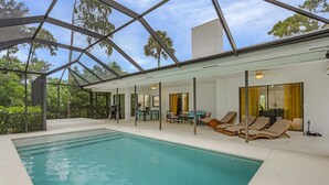 Una piscina interior moderna con paredes de vidrio transparente, sillones de descanso y un ventilador de techo.