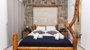 Una camera da letto con parete in pietra, testiera in legno, un letto con biancheria da letto bianco e marrone e due comodini con lampade.