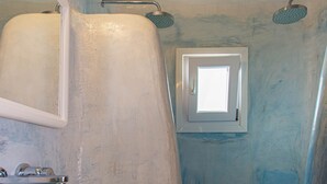 Un bagno con lavandino bianco, uno specchio, una doccia con una piccola finestra e un pavimento piastrellato.