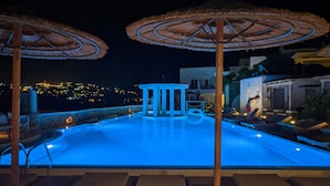 Area piscina notturna con sedie a sdraio e ombrelloni, circondata da muri in pietra e con vista sulla città.