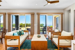 A spacious living area with a sofa, chairs, a coffee table, and large sliding glass doors leading to an outdoor patio. - Ocean Views! Kumulani D2. (Mauna Kea Resort)