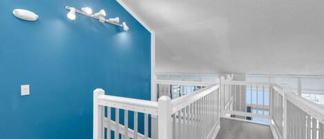 Un escalier avec des rampes blanches, un mur bleu et un luminaire au plafond.
