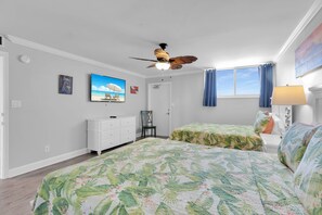 Un dormitorio con cama, cómoda, ventilador de techo, ventana con cortinas y un cuadro en la pared.