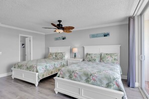 Ein Schlafzimmer mit zwei weißen Betten, einem Deckenventilator und einem Fenster mit Vorhängen.