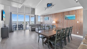 A spacious living area with a large wooden dining table, a gray sofa, and a view of the city through large windows.