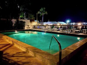 Ein Poolbereich bei Nacht mit Liegestühlen und Blick auf den Yachthafen.