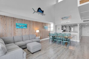 A spacious living area with a gray sectional sofa, a dining table with teal chairs, and wooden paneling on the walls. - Waterfront Dock Pool Pet Friendly Near Duval St (Key West)