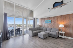 Amplia sala de estar con un sofá seccional gris, un pequeño reposapiés y una pared de madera decorativa con una obra de arte enmarcada.