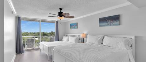 Un dormitorio con una cama grande, un ventilador de techo, vistas al exterior y un cuadro en la pared.