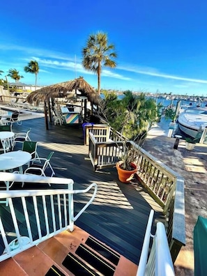 A wooden deck with outdoor seating, a thatched-roof structure, and a view of the marina with boats. - Waterfront Condo + Pool Downtown + Boat Slip (Key West)