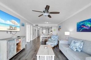 Un salon doté d’un ventilateur de plafond, d’une grande télévision, d’un canapé, d’une table basse et d’un coin repas avec des chaises et une table.