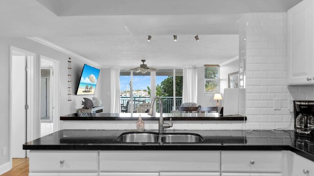 A modern kitchen with white cabinetry, black countertops, a stainless steel sink, and a view of the outdoors. - Waterfront Condo Dock Pool Downtown Near Duval (Key West)