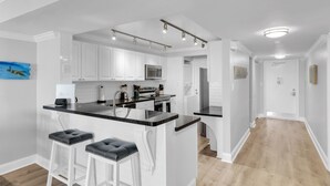 A modern kitchen with white cabinetry, a black countertop, and three bar stools. - Waterfront Condo Dock Pool Downtown Near Duval (Key West)