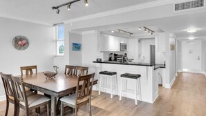 A modern kitchen with white cabinets, a central island with stools, and a dining area with wooden chairs. - Waterfront Condo Dock Pool Downtown Near Duval (Key West)