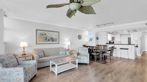 A spacious living room with a wooden floor, a ceiling fan, a dining area with a kitchen in the background, and a large painting on the wall. - Waterfront Condo Dock Pool Downtown Near Duval (Key West)