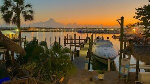 A marina at dusk with a boat docked, palm trees, and a thatched-roof building. - Waterfront Condo Dock Pool Downtown Near Duval (Key West)