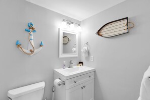 A bathroom with a toilet, sink, and mirror. There is a decorative anchor on the wall and a small boat decoration. - Waterfront Condo | Pool, Dock, Parking, Sleeps 8 (Key West)