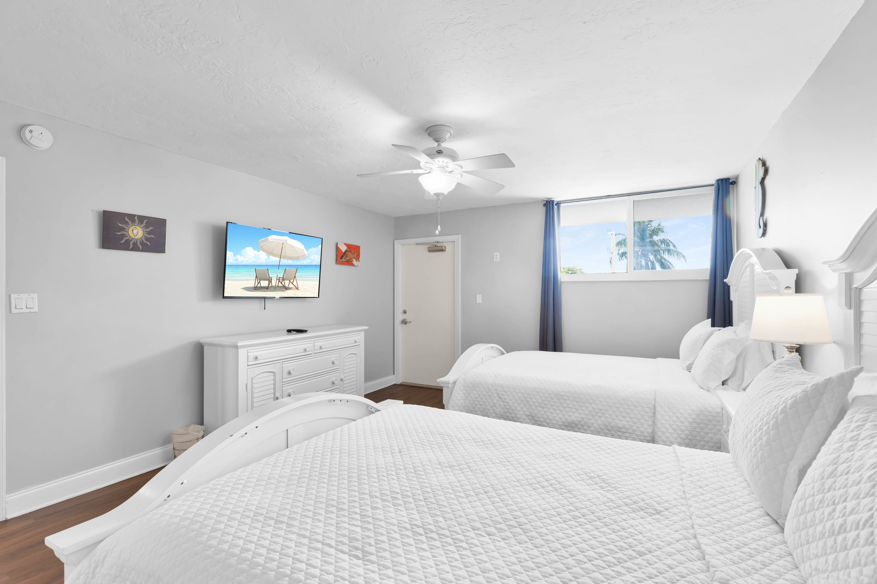 Une chambre d’hôtel avec un lit, un bureau, un ventilateur de plafond et une fenêtre avec des rideaux.