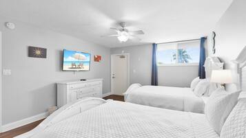 Une chambre d’hôtel avec un lit, un bureau, un ventilateur de plafond et une fenêtre avec des rideaux.