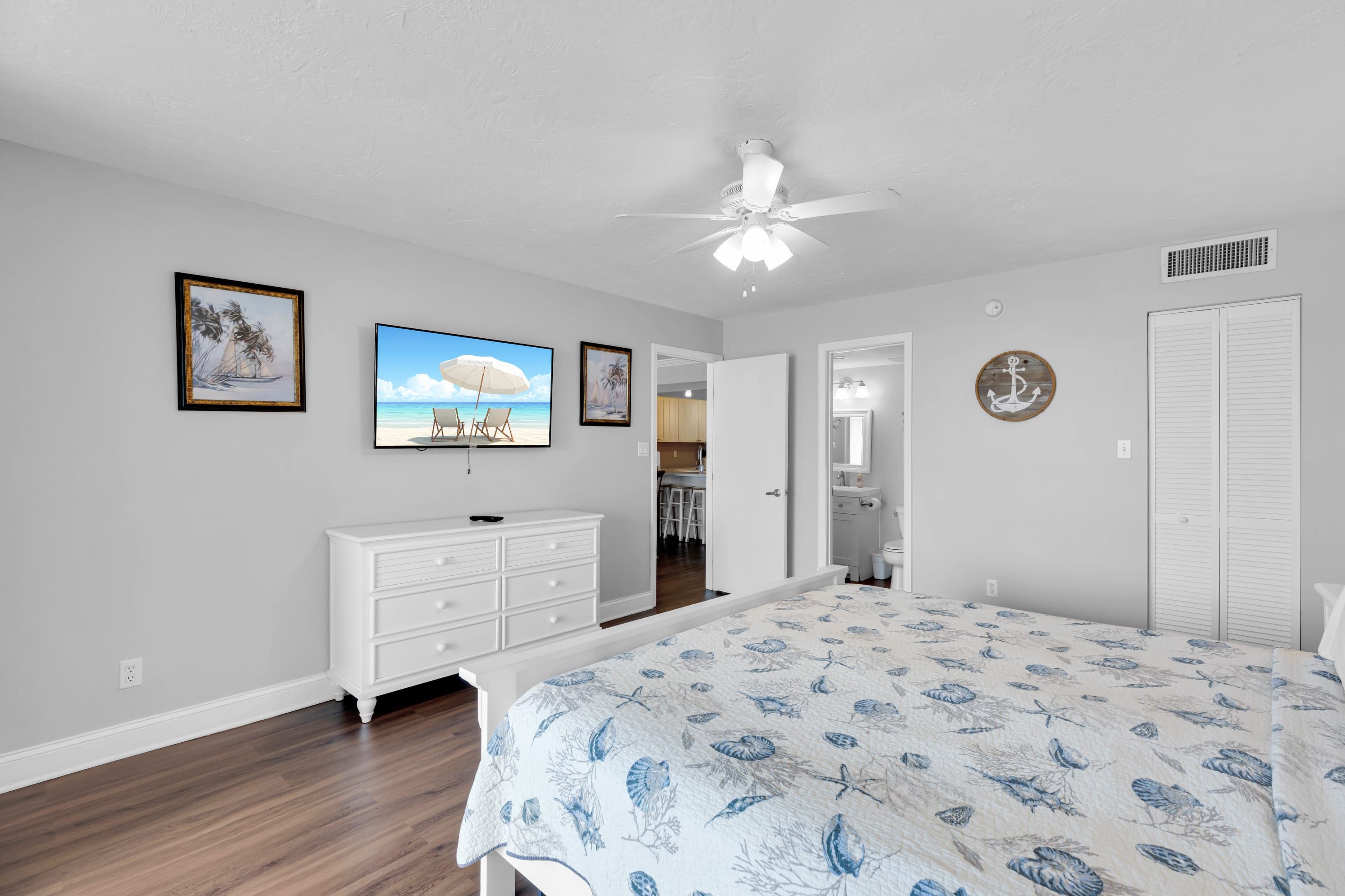 A bedroom with a bed, dresser, ceiling fan, and artwork on the wall.