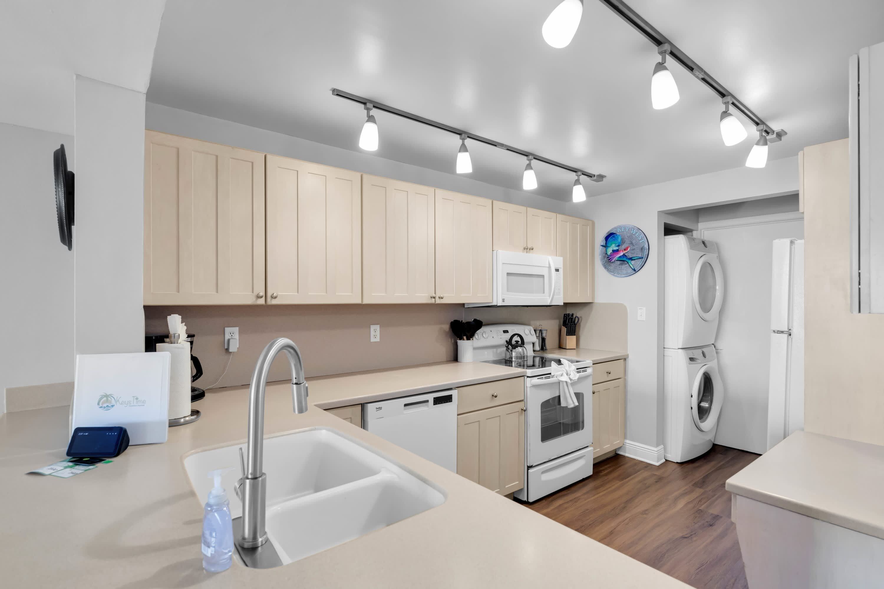 A modern kitchen with a built-in dishwasher, a microwave, and a stove. There is a sink with a faucet and a countertop with a bottle of hand soap.
