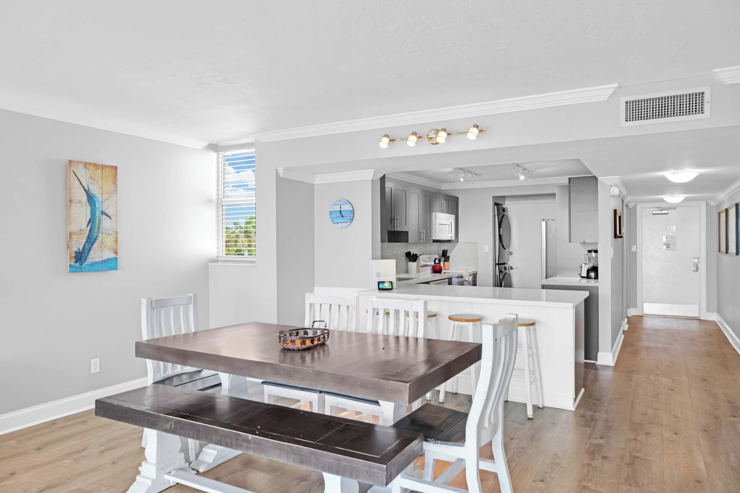 A modern kitchen with white cabinets, a central island, and a dining area with a wooden table and white chairs.