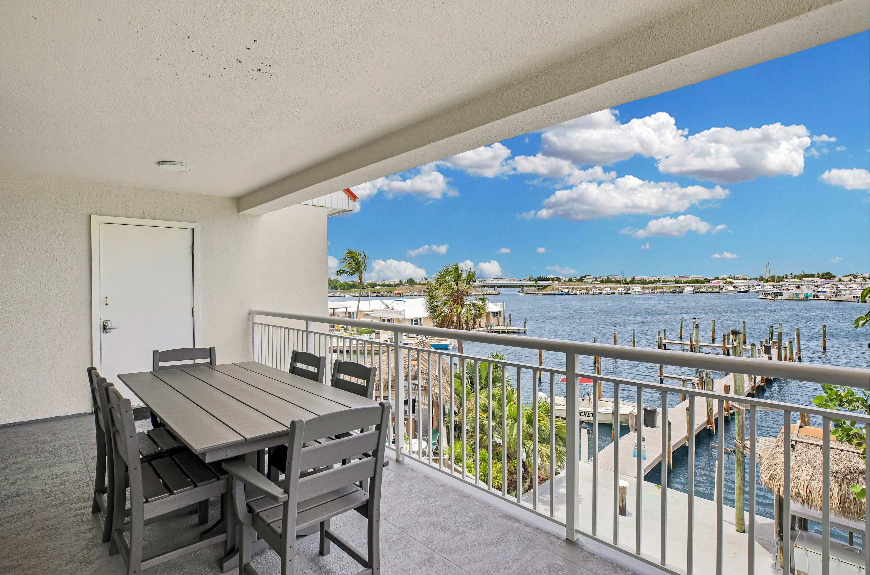 A balcony with a table and chairs, overlooking a marina with boats and a clear sky.