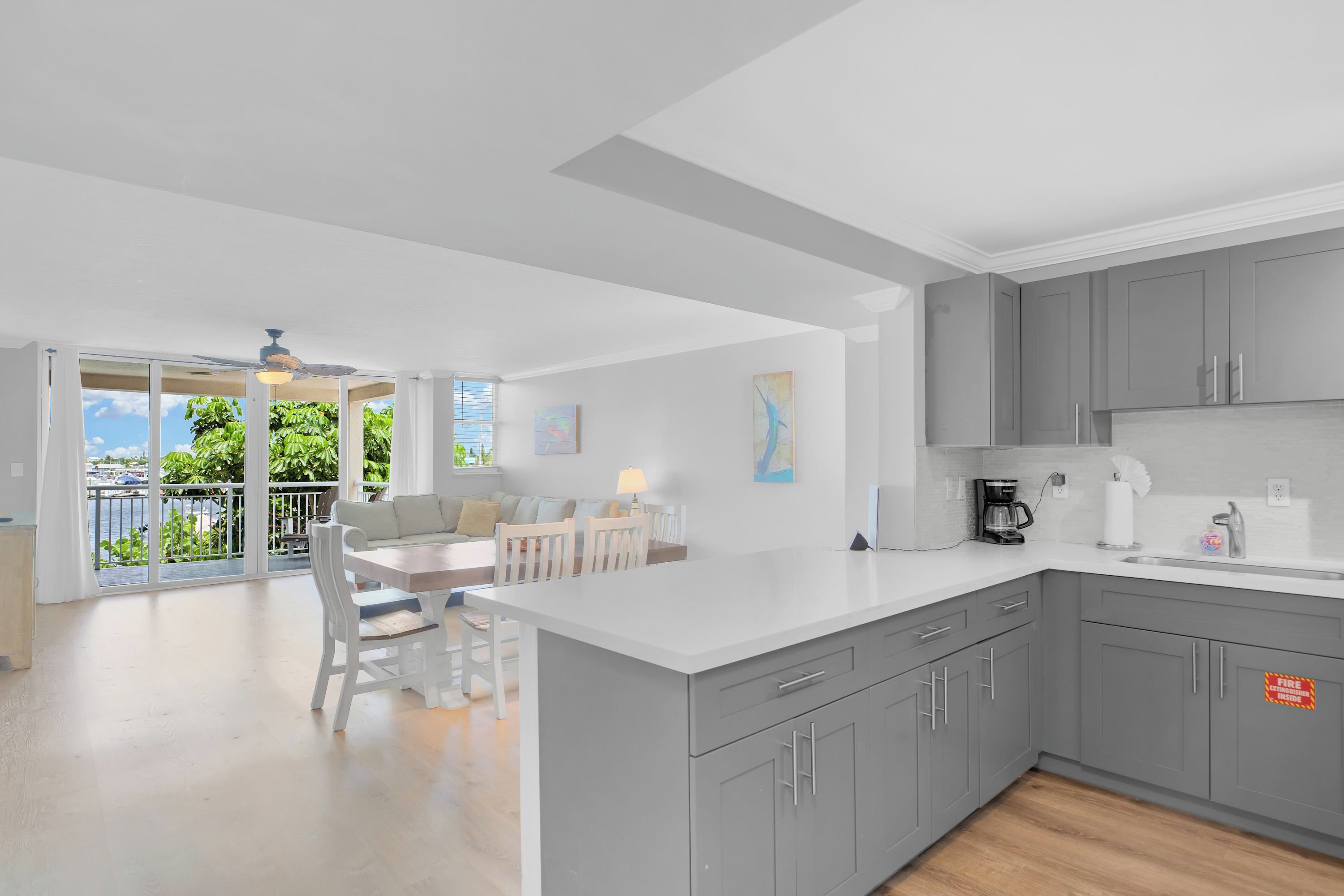 A modern kitchen with grey cabinets, a white countertop, and a dining area with a table and chairs.
