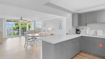 A modern kitchen with grey cabinets, a white countertop, and a dining area with a table and chairs.