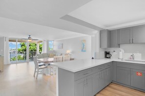 A modern kitchen with grey cabinets, a white countertop, and a dining area with a table and chairs.