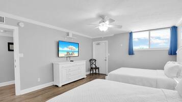 Ein Schlafzimmer mit zwei Betten, einem Deckenventilator, einem an der Wand befestigten Fernseher und einem Fenster mit Vorhängen.
