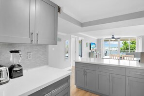 A modern kitchen with grey cabinets, a white countertop, and a blender. There is a view of a balcony with a chair and a table.