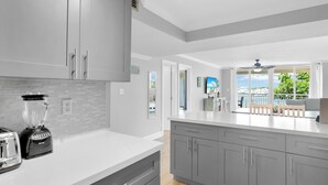 A modern kitchen with grey cabinets, a white countertop, and a blender. There is a view of a balcony with a chair and a table. - Waterfront Dock Pool Key West Near Duval (Key West)