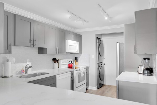 A modern kitchen with grey cabinets, a white countertop, stainless steel appliances, and a built-in microwave.