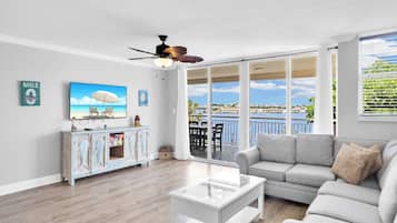 A spacious living room with a large window overlooking a scenic view, a ceiling fan, and a modern white coffee table.
