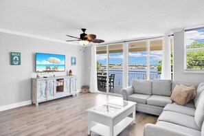 A spacious living room with a large window overlooking a scenic view, a ceiling fan, and a modern white coffee table.