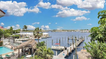 A marina with docked boats, a swimming pool with lounge chairs, and a view of the water and distant buildings.