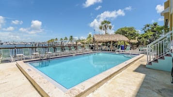 A rectangular swimming pool with a clear blue water, surrounded by lounge chairs and a thatched-roof structure.